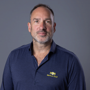 Porträtfoto von Markus Stoll, der ein dunkelblaues Poloshirt mit gelbem Logo trägt.
